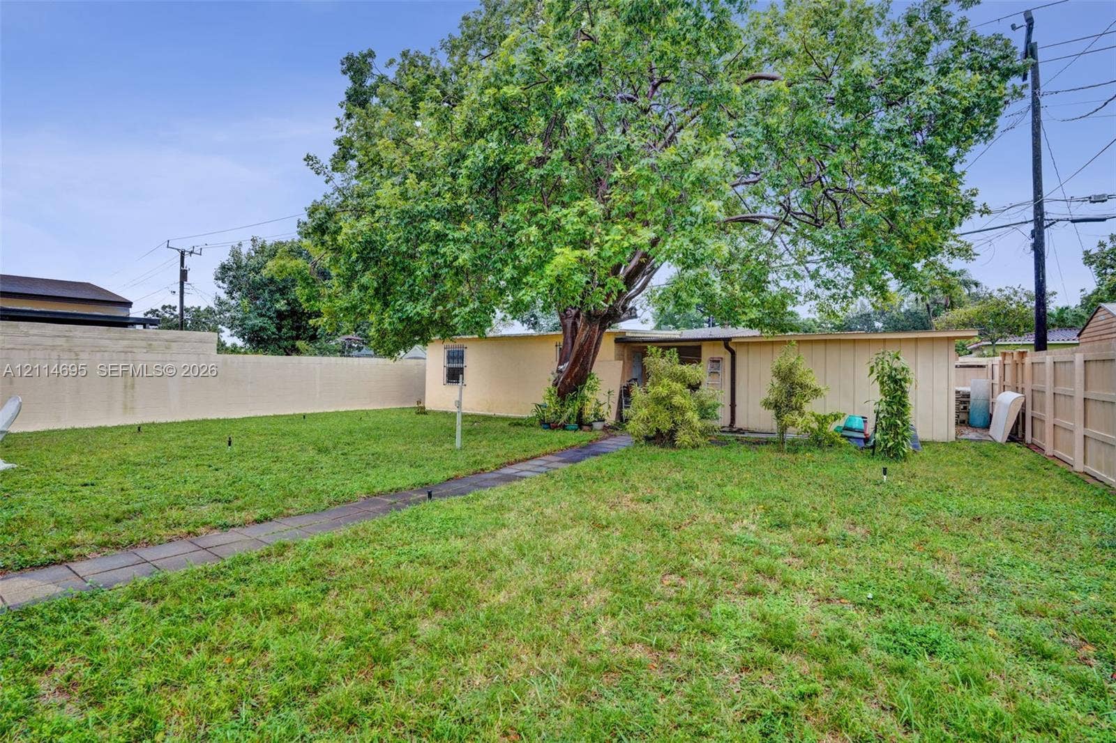 Backyard featuring a sprawling lawn, a large mature tree, a paved stone pathway, and perimeter privacy fencing
