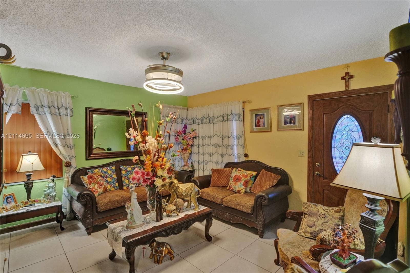 Living area featuring large format ceramic tile flooring, a modern circular LED flush-mount ceiling fan, and a wood entry door with an oval decorative glass insert