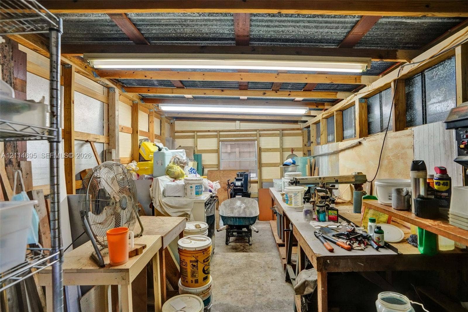 Workshop space featuring exposed timber framing, concrete flooring, corrugated metal ceiling panels, and integrated overhead fluorescent lighting