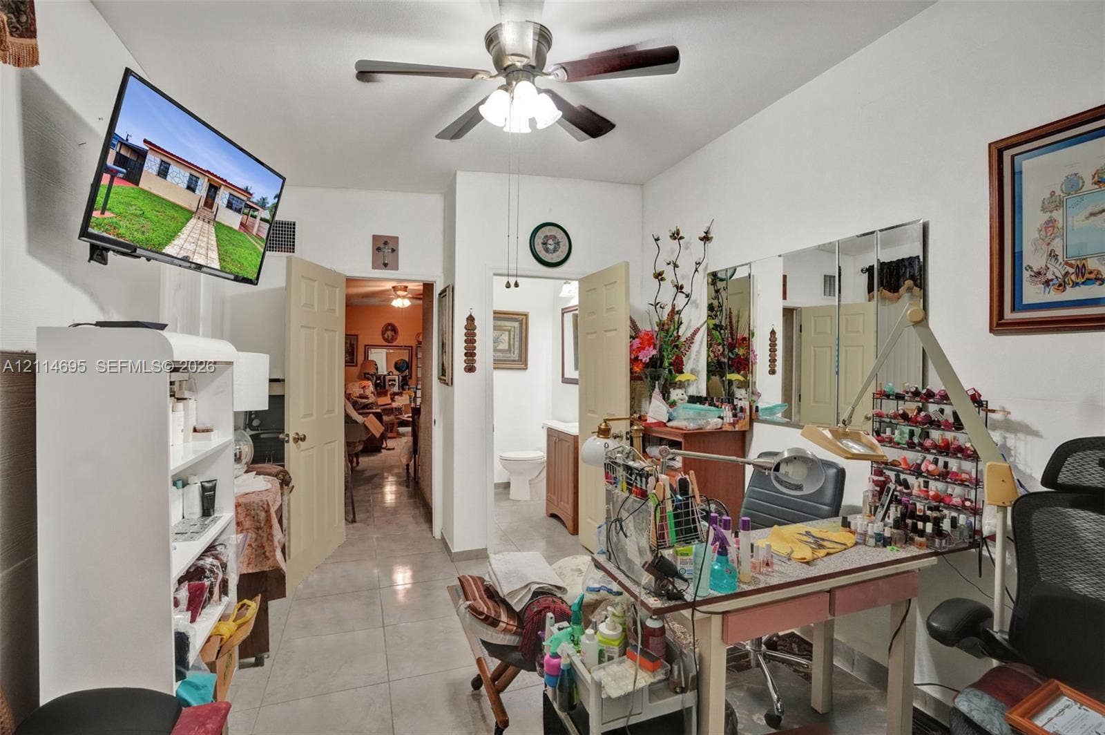 Room featuring tile flooring, a ceiling fan with integrated light fixture, multiple six-panel interior doors, and wall-mounted vanity mirrors