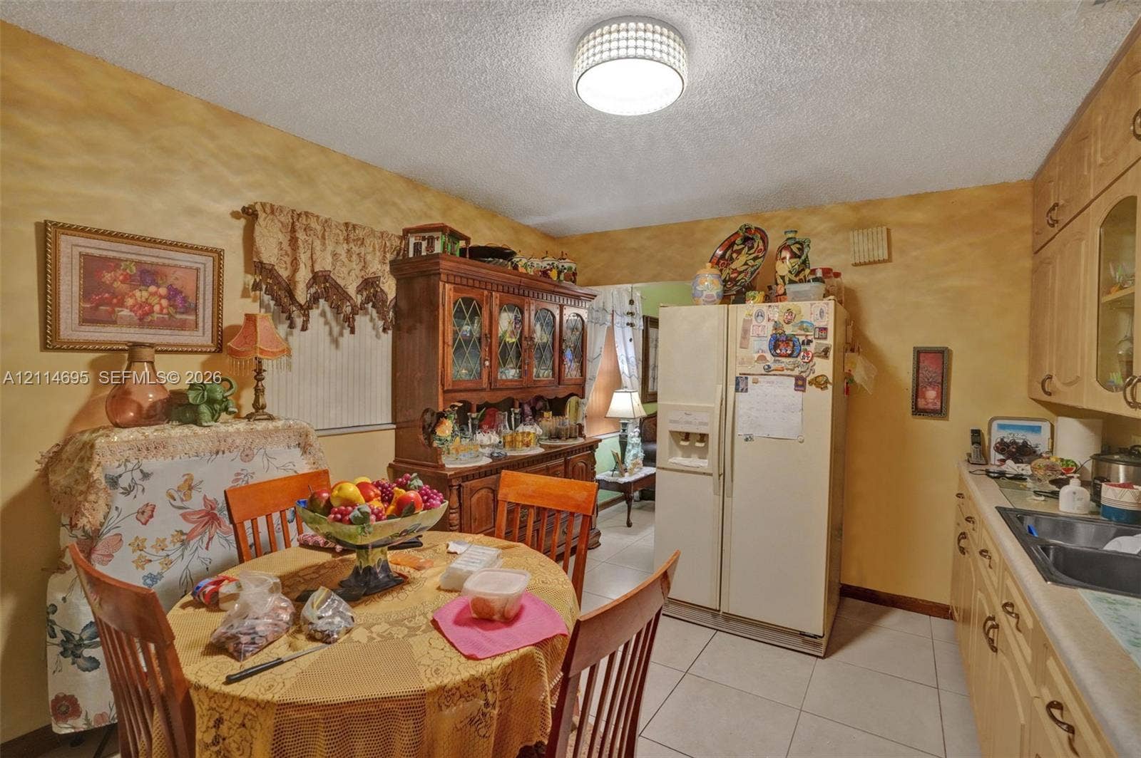 Kitchen featuring light-finish wood cabinetry, a dual-basin sink, tile flooring, and a glass-front display cabinet