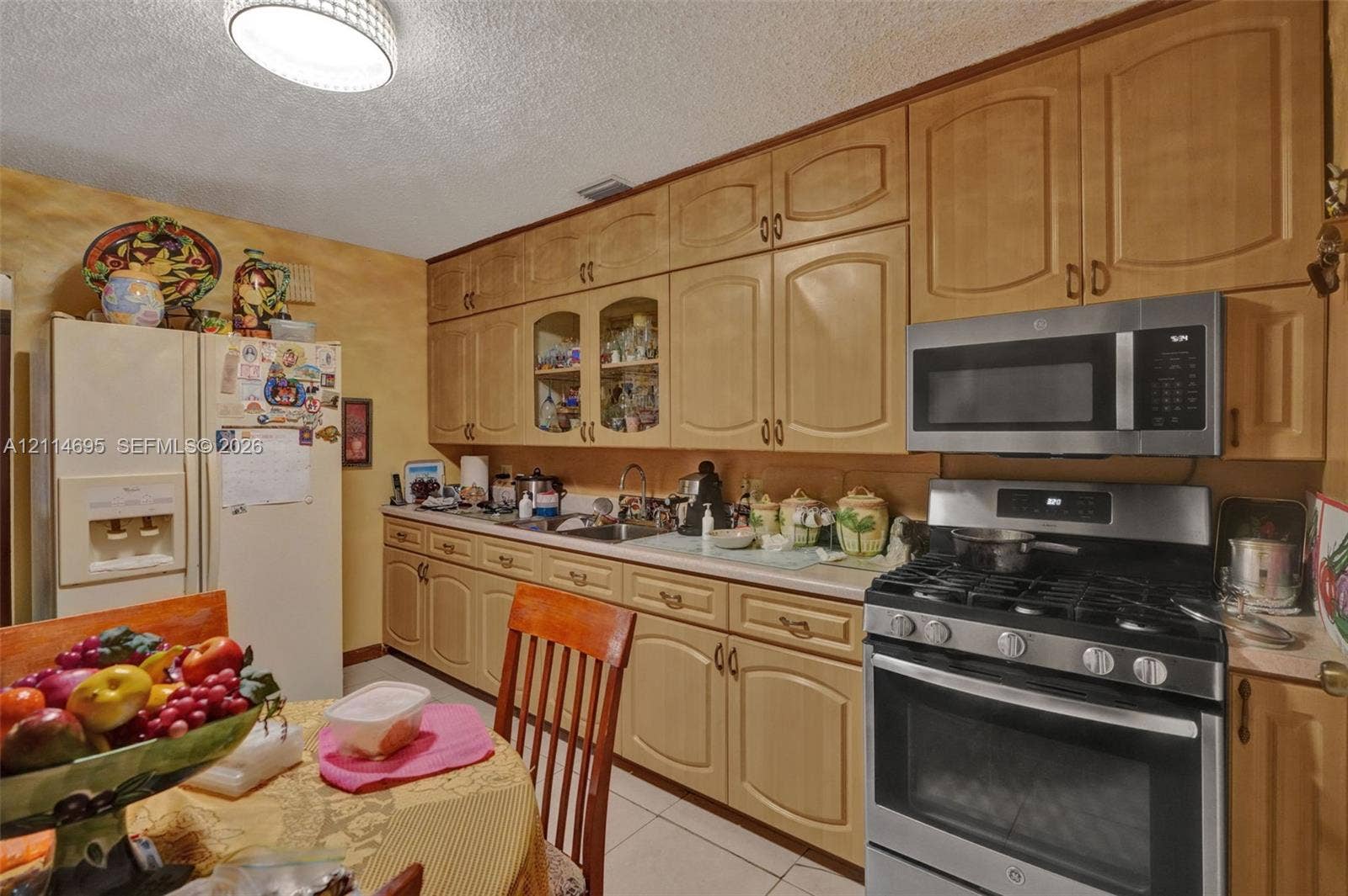 Kitchen featuring extensive light-toned wood cabinetry with glass-front display accents, stainless steel gas range, over-the-range microwave, and tile flooring