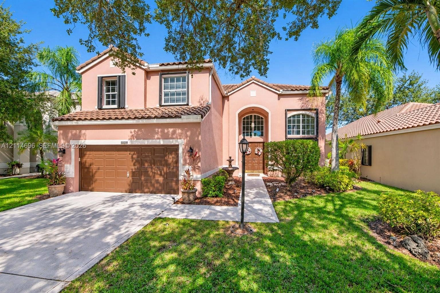 Two-story stucco exterior featuring a tile roof, arched entryway, multi-paned windows, and a concrete driveway leading to an attached two-car garage