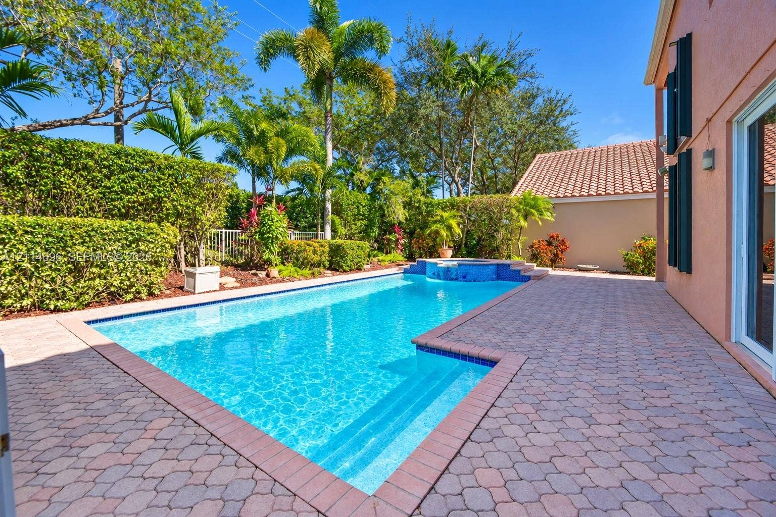 In-ground swimming pool with a raised spillover spa, expansive paver patio, and privacy hedges