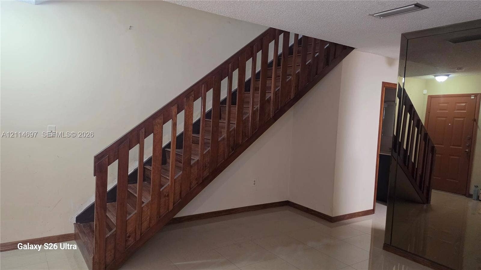 121 SW 113th Avenue, #104-10, Sweetwater, Sweetwater, FL 33174 Staircase featuring stained wood treads and a slatted wood balustrade, paired with mirrored wall paneling and polished tile flooring