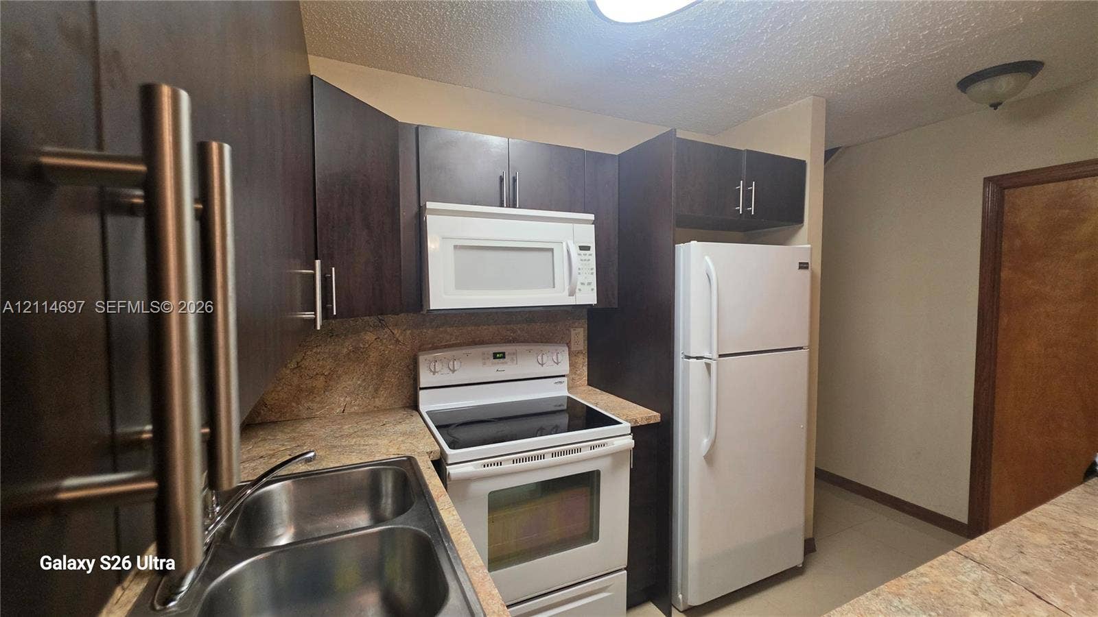121 SW 113th Avenue, #104-10, Sweetwater, Sweetwater, FL 33174 Kitchen featuring dark-toned cabinetry, stone-finish countertops, stainless steel dual-basin sink, and white appliances including a built-in microwave and range