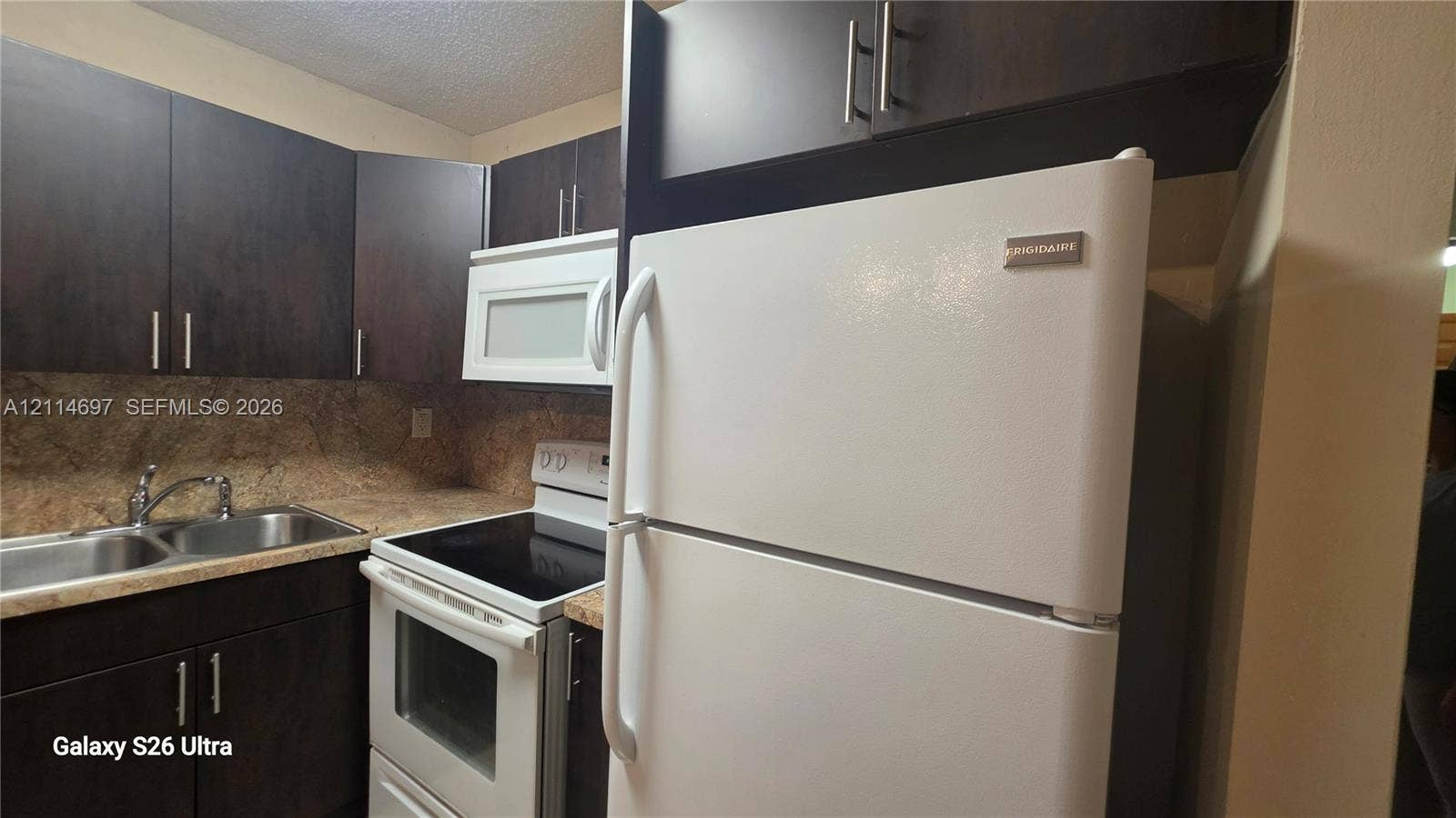 121 SW 113th Avenue, #104-10, Sweetwater, Sweetwater, FL 33174 Dark wood-finish cabinetry, white appliances, stone-patterned laminate countertops, and stainless steel dual-basin sink with a gooseneck faucet