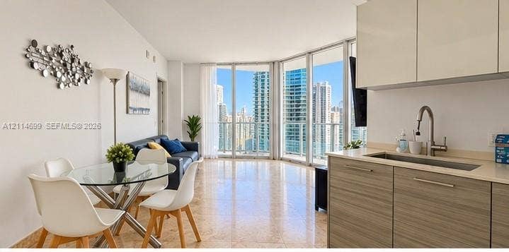 1300 Brickell Bay Drive, #3007, Miami, FL 33131 Open-concept living space featuring floor-to-ceiling windows, polished stone flooring, high-gloss upper cabinetry, and wood-finish lower kitchen cabinetry with a stainless steel undermount sink