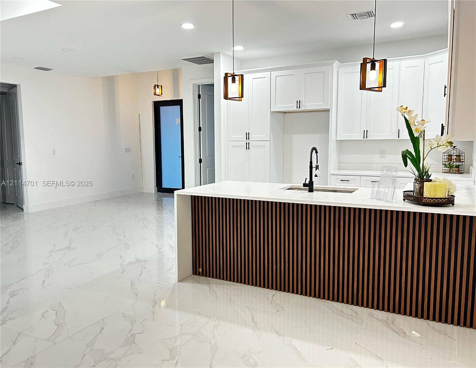 Kitchen featuring white cabinetry, an island with a wood-slat base and light-toned countertop, matte black fixtures, recessed lighting, and large-format tile flooring