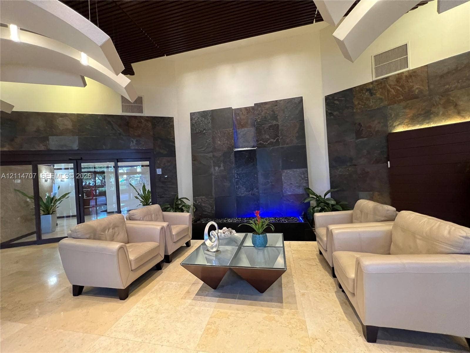 3300 NE 191st Street, #1405, Aventura, Aventura, FL 33180 Lobby area featuring tile flooring, stone-clad accent walls, a built-in water feature, and a vaulted ceiling with architectural lighting