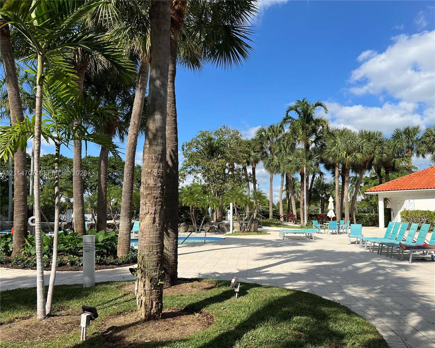 3300 NE 191st Street, #1405, Aventura, Aventura, FL 33180 Outdoor terrace featuring light-toned paved hardscaping, mature palm trees, manicured landscaping, and a red-tiled roof structure