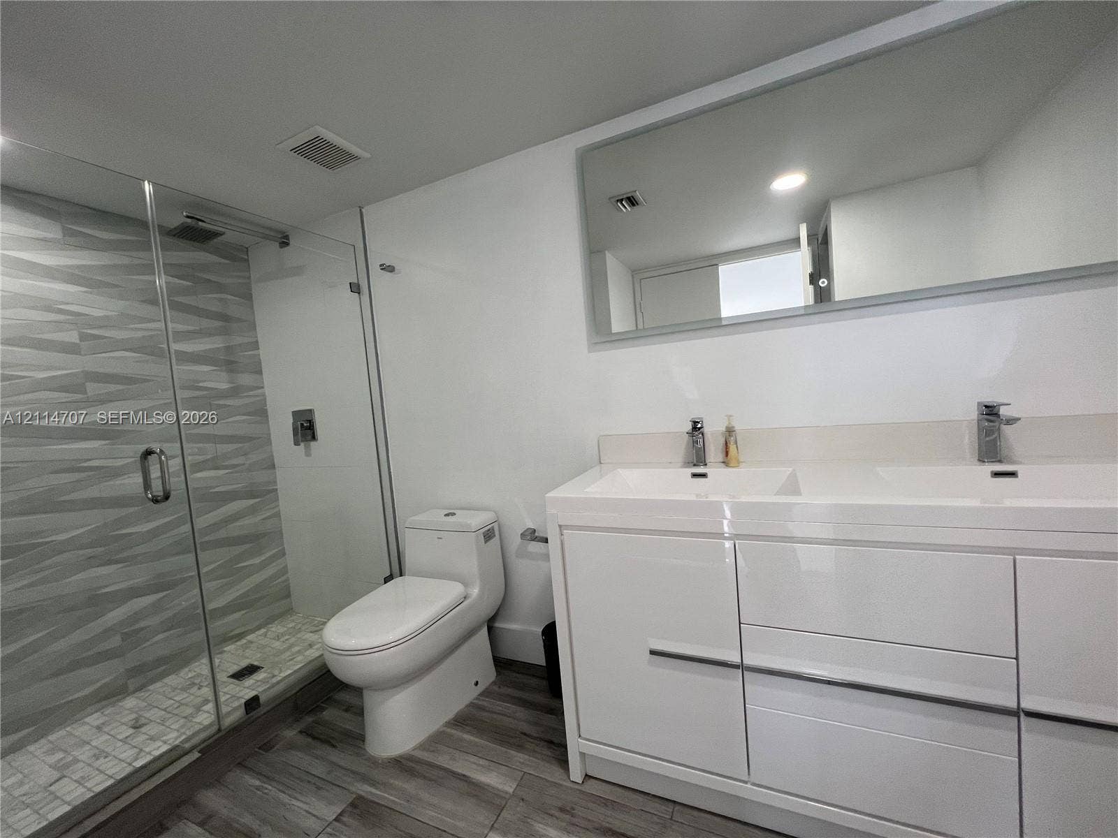 3300 NE 191st Street, #1405, Aventura, Aventura, FL 33180 Double vanity with integrated sinks, glass-enclosed shower featuring textured wall tile, mosaic tile shower floor, and wood-finish flooring