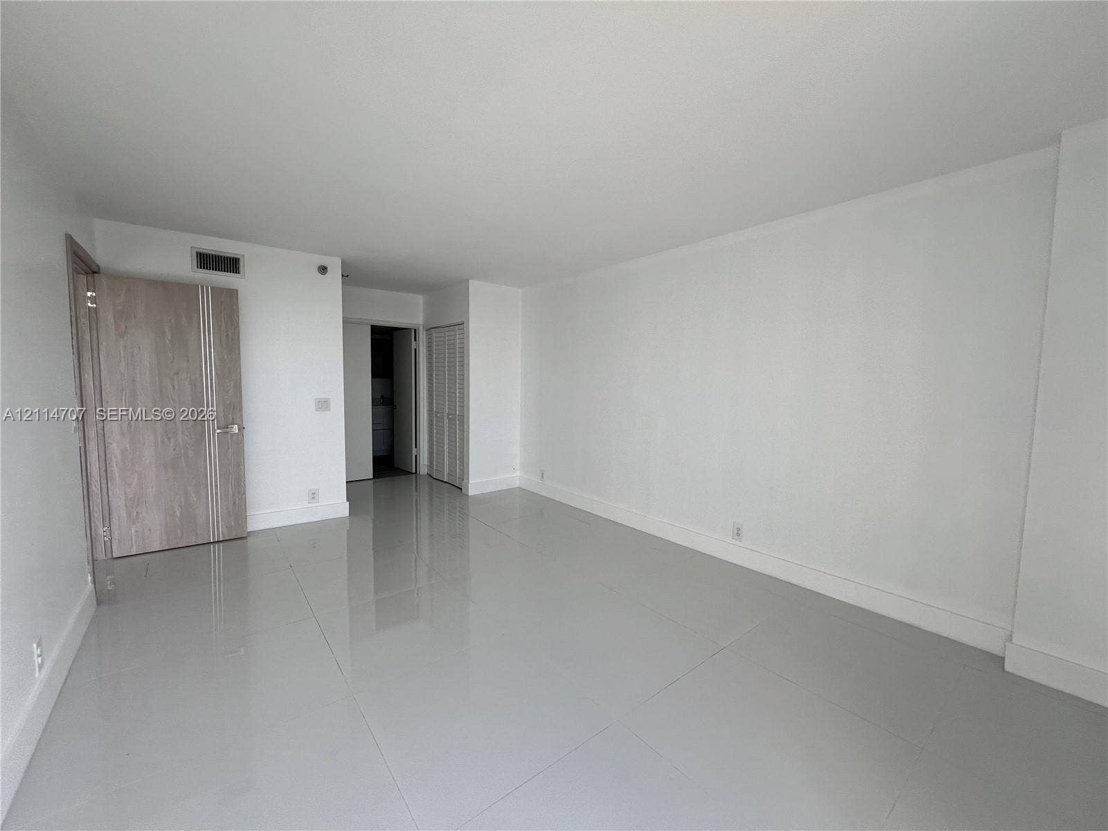 3300 NE 191st Street, #1405, Aventura, Aventura, FL 33180 Open living area featuring large-format polished tile flooring, neutral wall finishes, a solid-core door with vertical detailing, and louvered closet doors