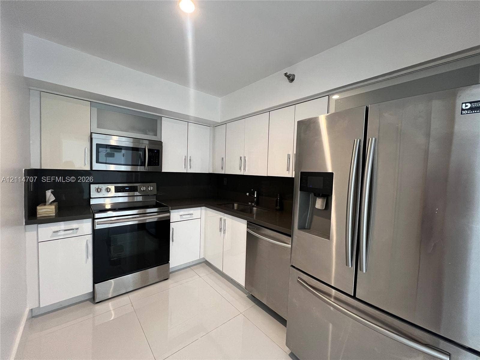 3300 NE 191st Street, #1405, Aventura, Aventura, FL 33180 Kitchen featuring white high-gloss cabinetry, dark solid-surface countertops, stainless steel appliances, and large-format tile flooring