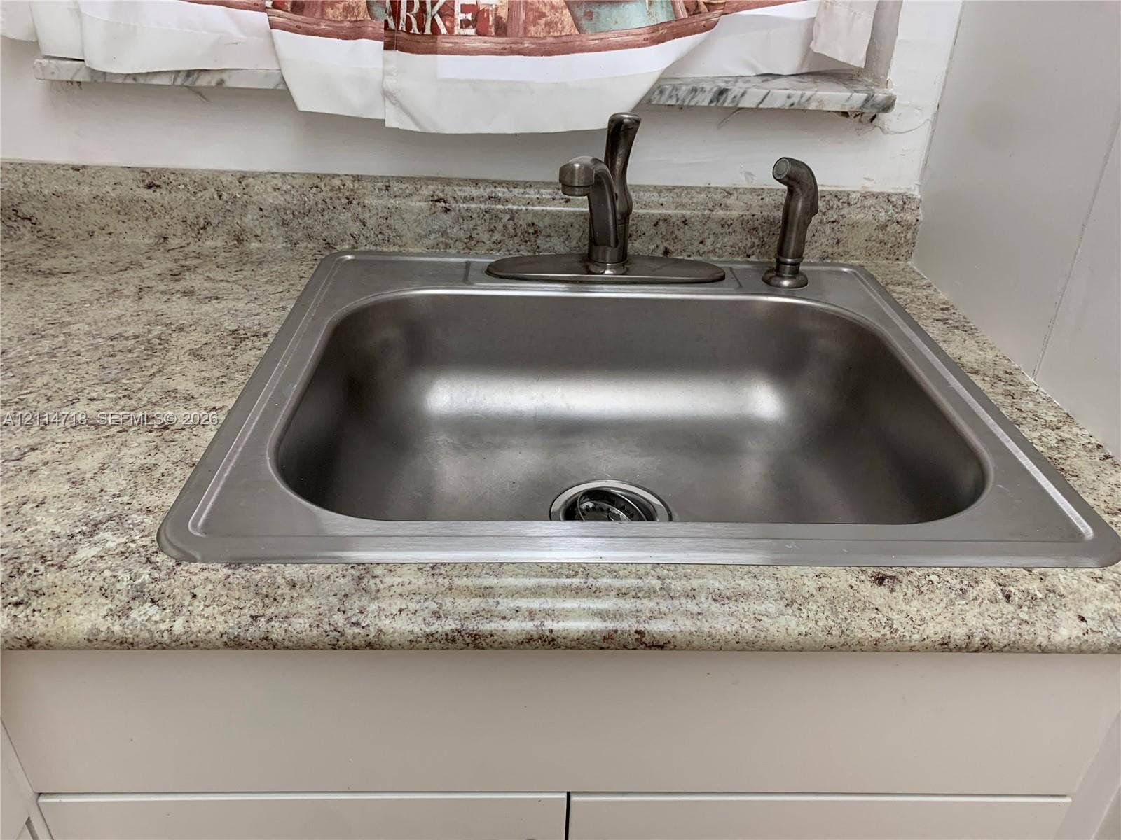 Stainless steel drop-in sink featuring a high-arc faucet, integrated side sprayer, and stone-finish countertop with matching backsplash