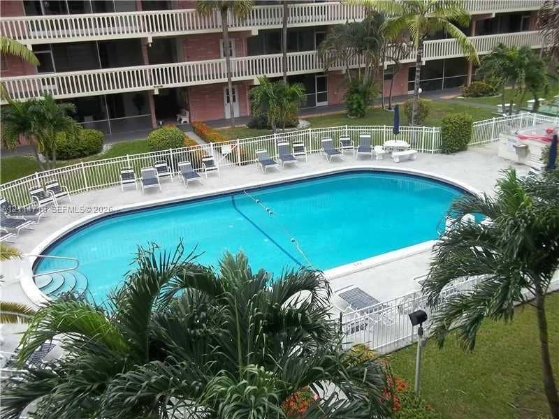 Outdoor swimming pool featuring a concrete deck, white perimeter fencing, and mature palm trees