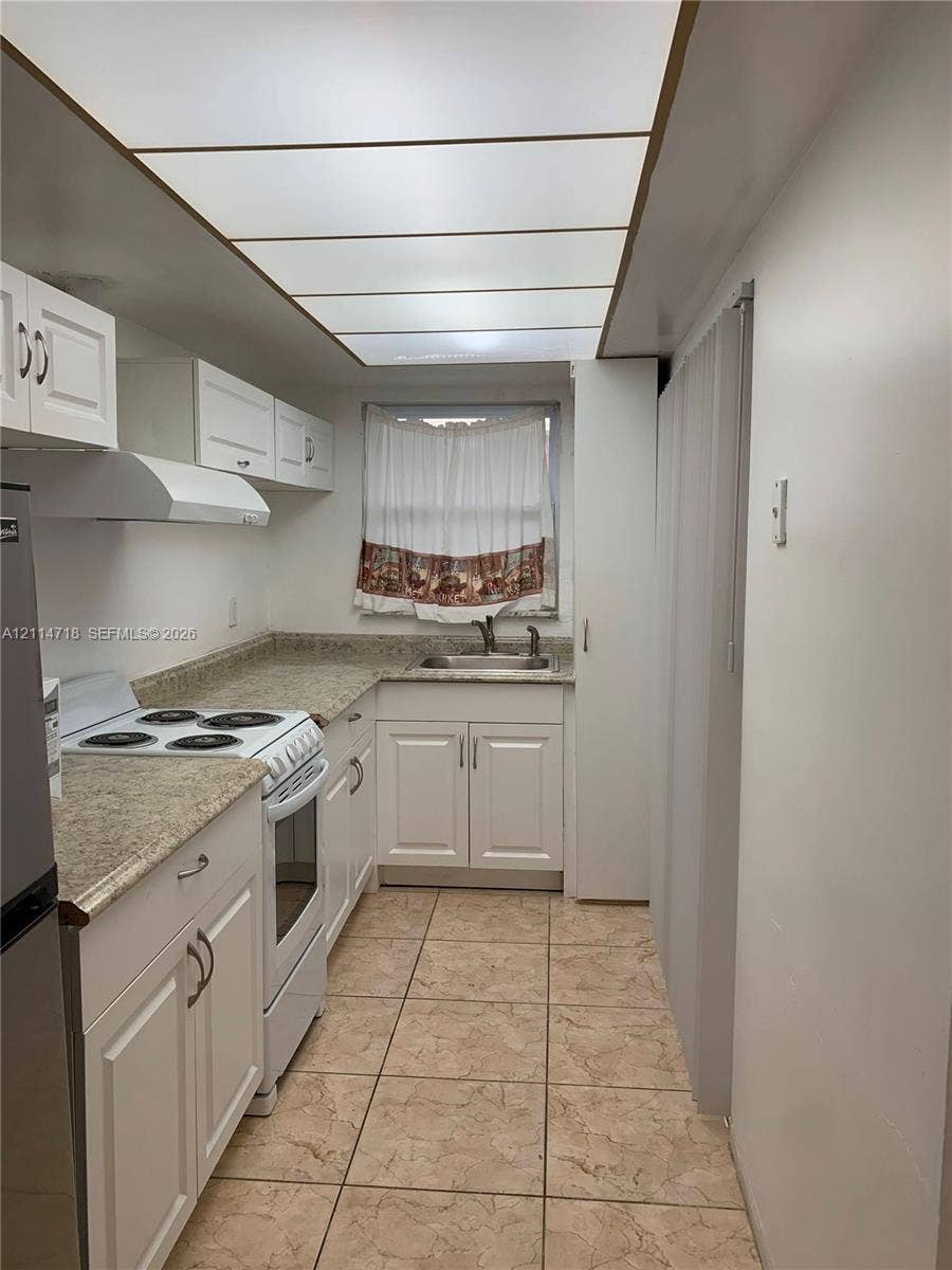 Kitchen featuring white cabinetry, stone-finish countertops, tile flooring, integrated ceiling panel lighting, and a metal sink with a faucet