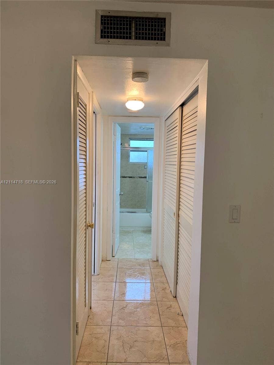 Hallway featuring floor-to-ceiling louvered closet doors, polished tile flooring, and flush-mount lighting