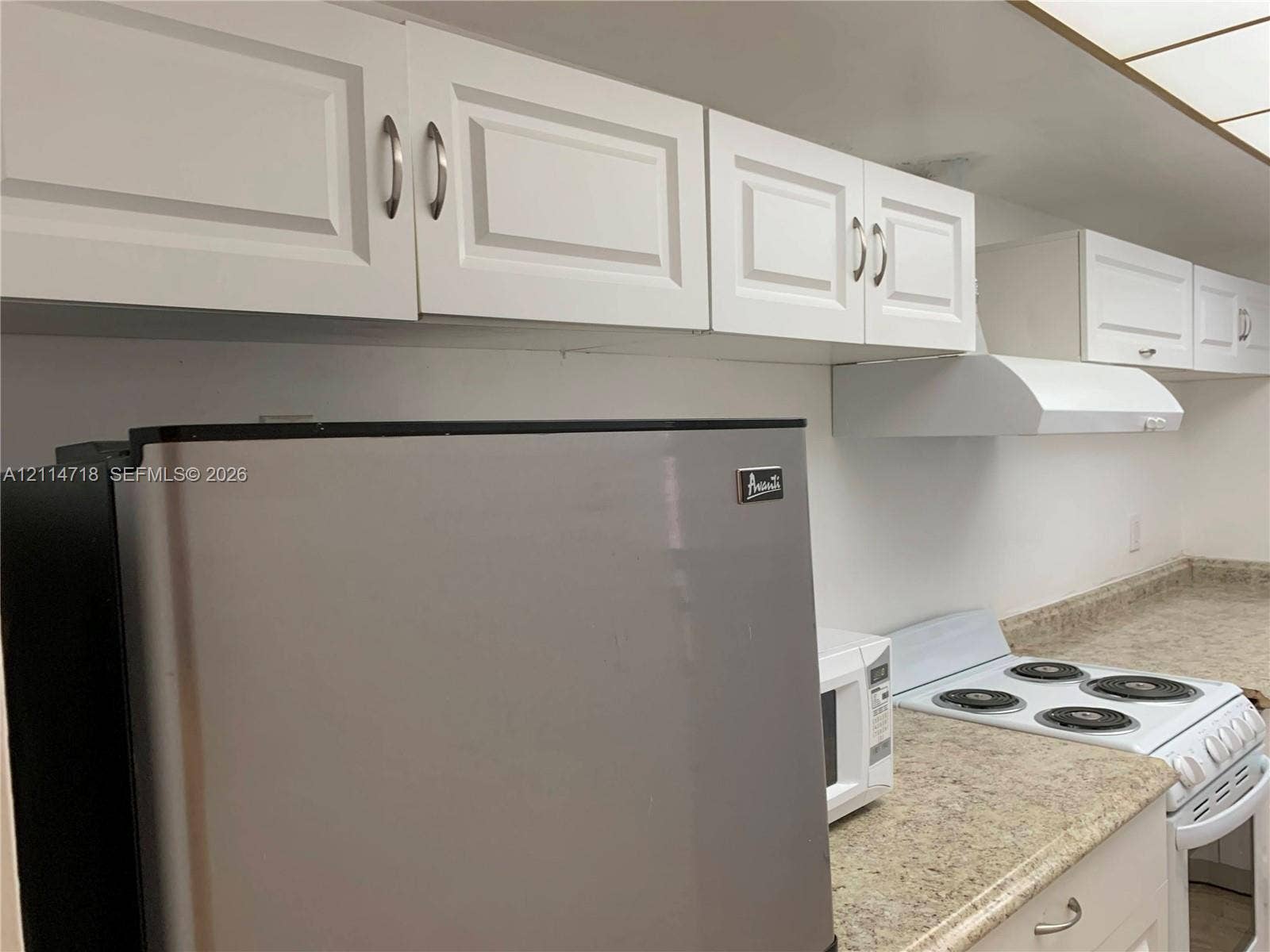 Kitchen featuring white shaker-style cabinetry, brushed nickel hardware, stone-patterned laminate countertops, and a white electric range with a matching range hood