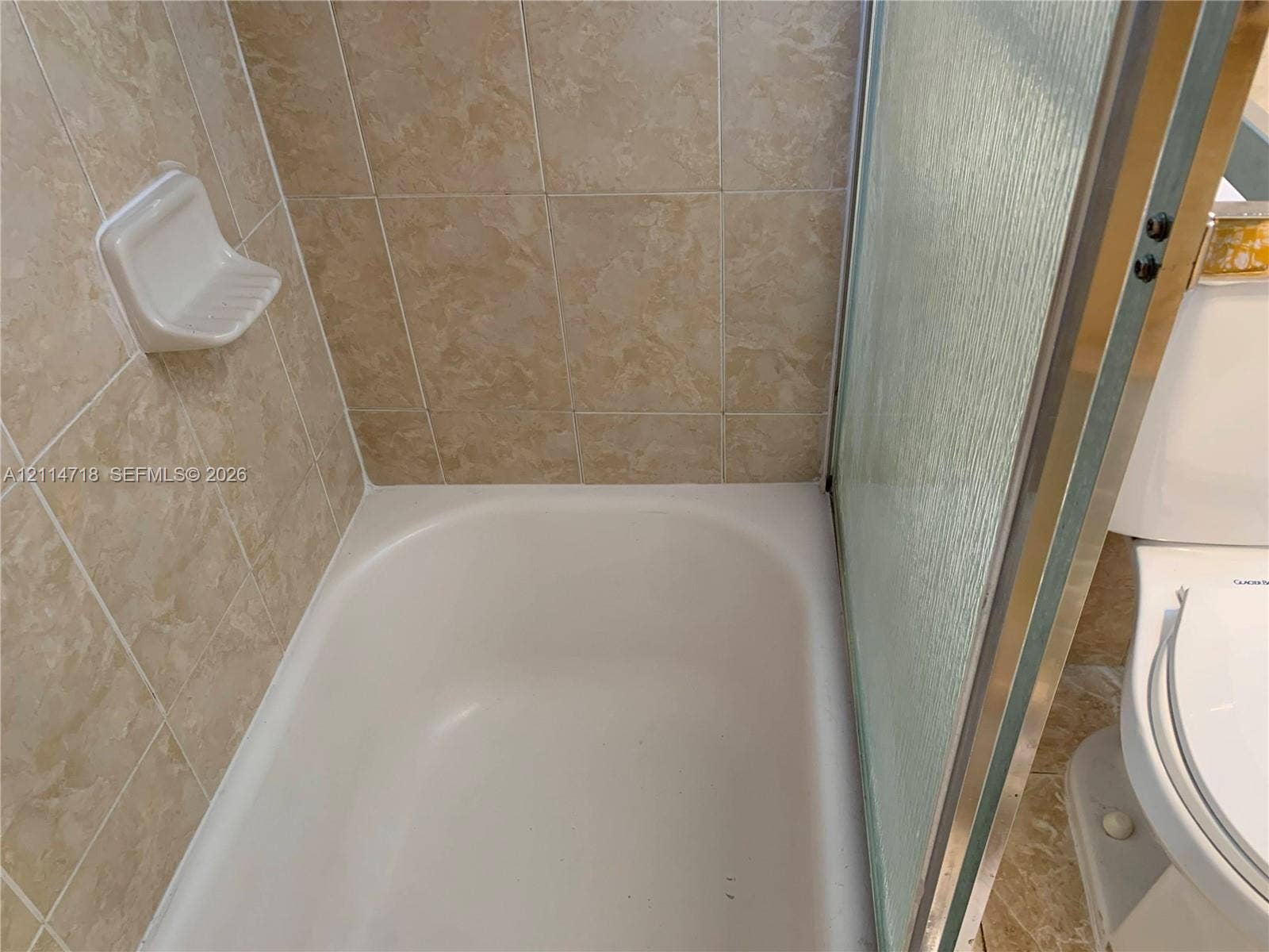 Bathtub with neutral-toned wall tiling, integrated soap dish, and glass sliding shower door