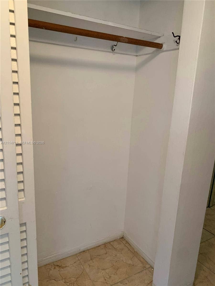 Closet featuring louvered bi-fold doors, a built-in upper shelf, a sturdy hanging rod, and stone-finish tile flooring