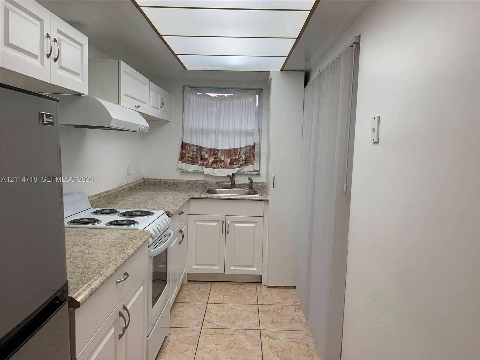 Kitchen featuring white shaker-style cabinetry, stone-finish countertops, tiled flooring, integrated drop-ceiling lighting, and a double-basin stainless steel sink