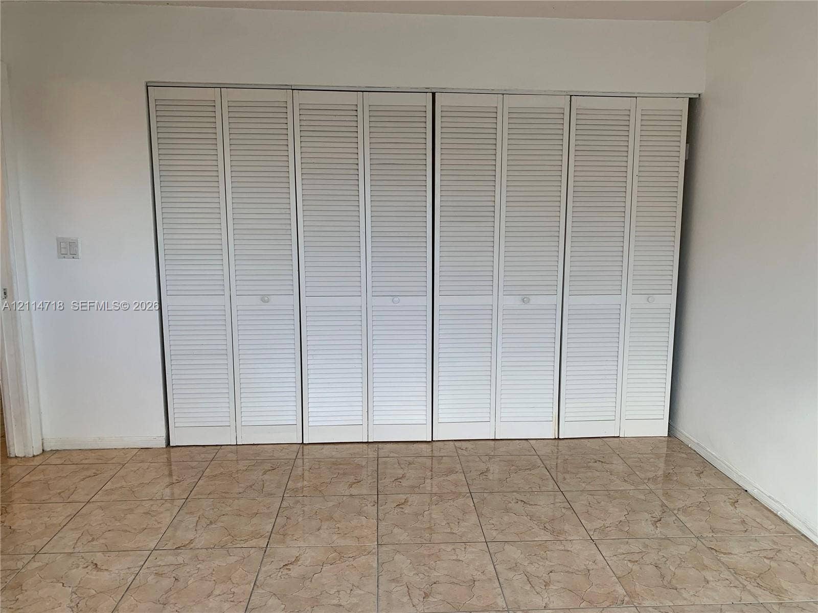 Wall-to-wall folding louvered closet doors and neutral tile flooring