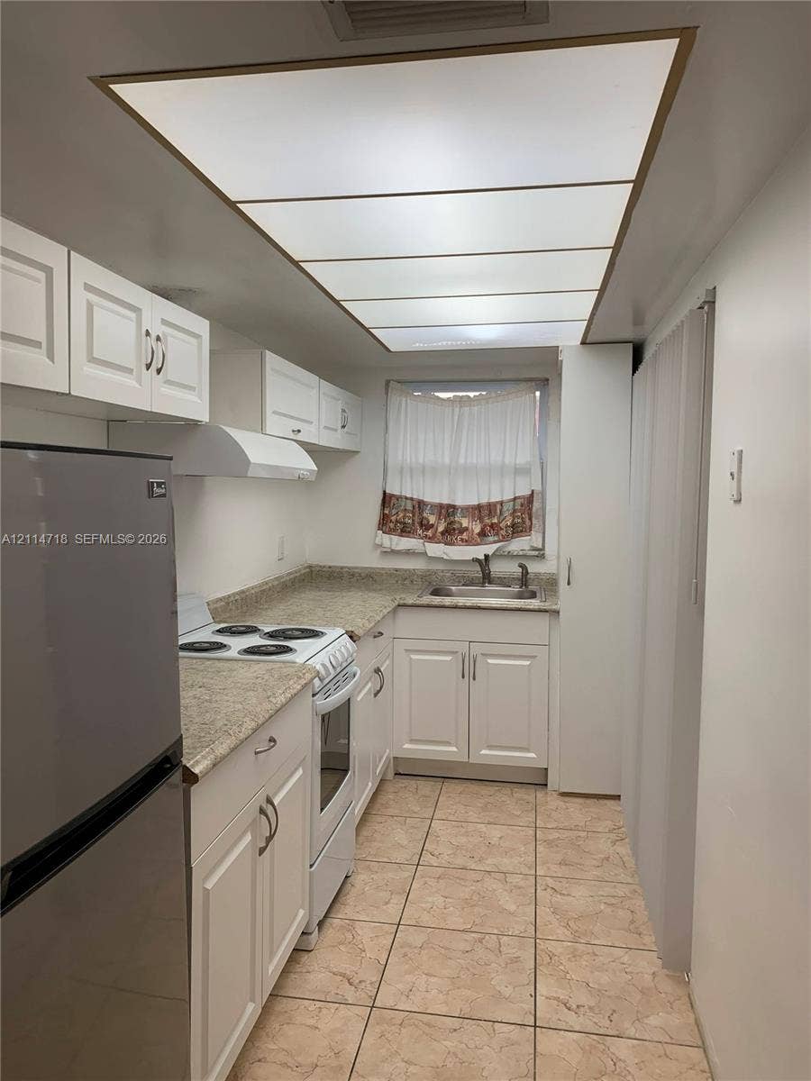 Kitchen featuring white cabinetry, stone-finish countertops, stainless steel sink, built-in range hood, and tile flooring