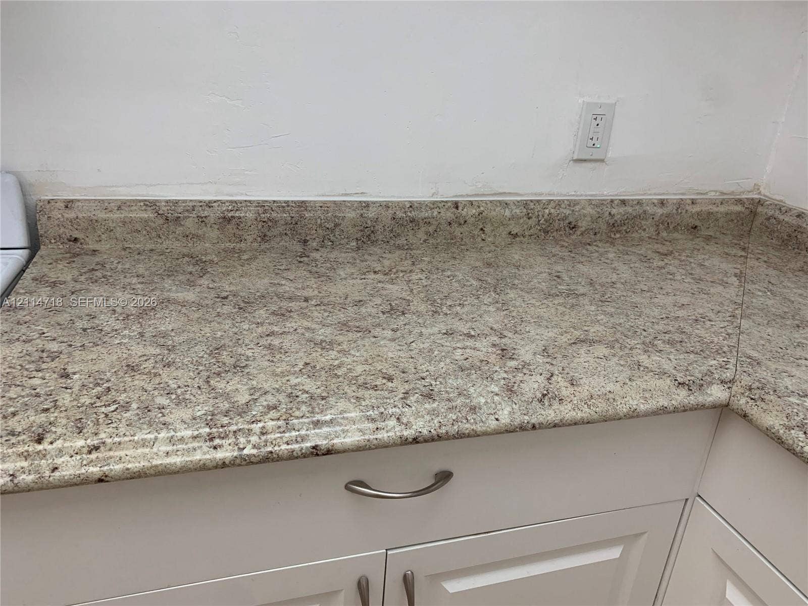 Speckled stone-finish countertop with integrated backsplash and white cabinetry featuring brushed metal pulls