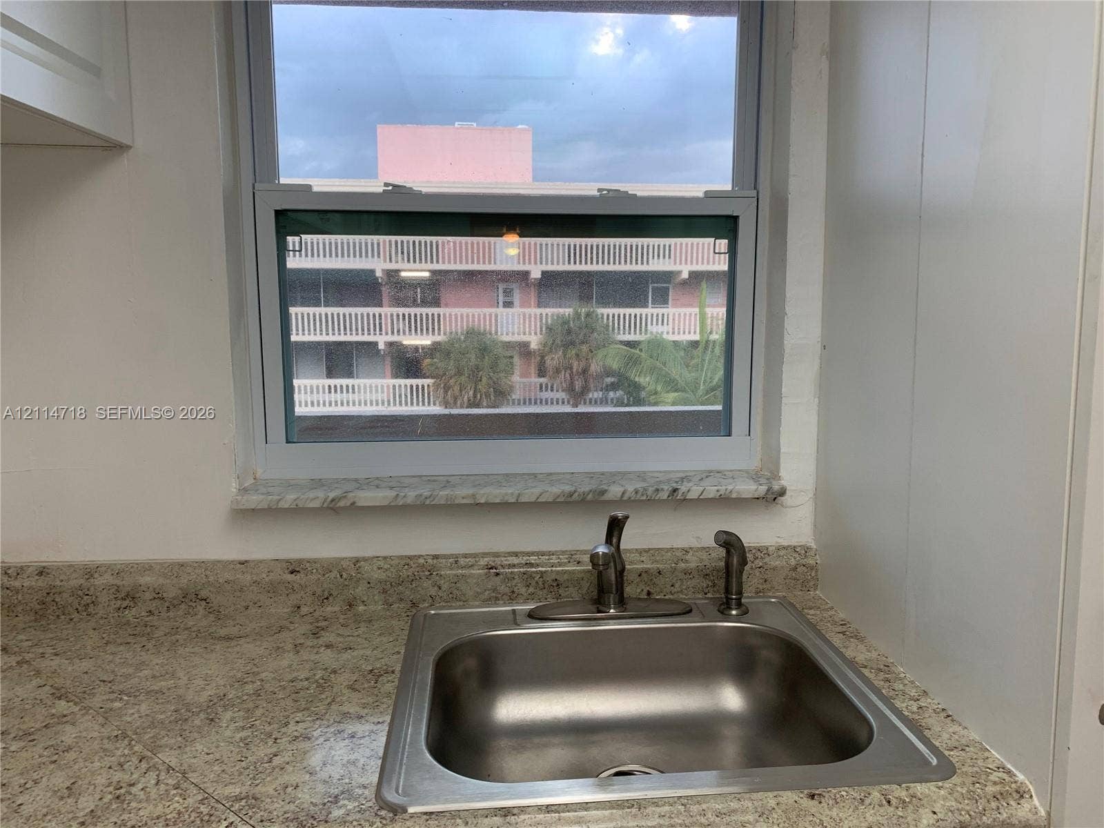 Single-basin stainless steel sink with high-arch faucet, set into a stone-finish countertop with integrated backsplash and a stone window sill