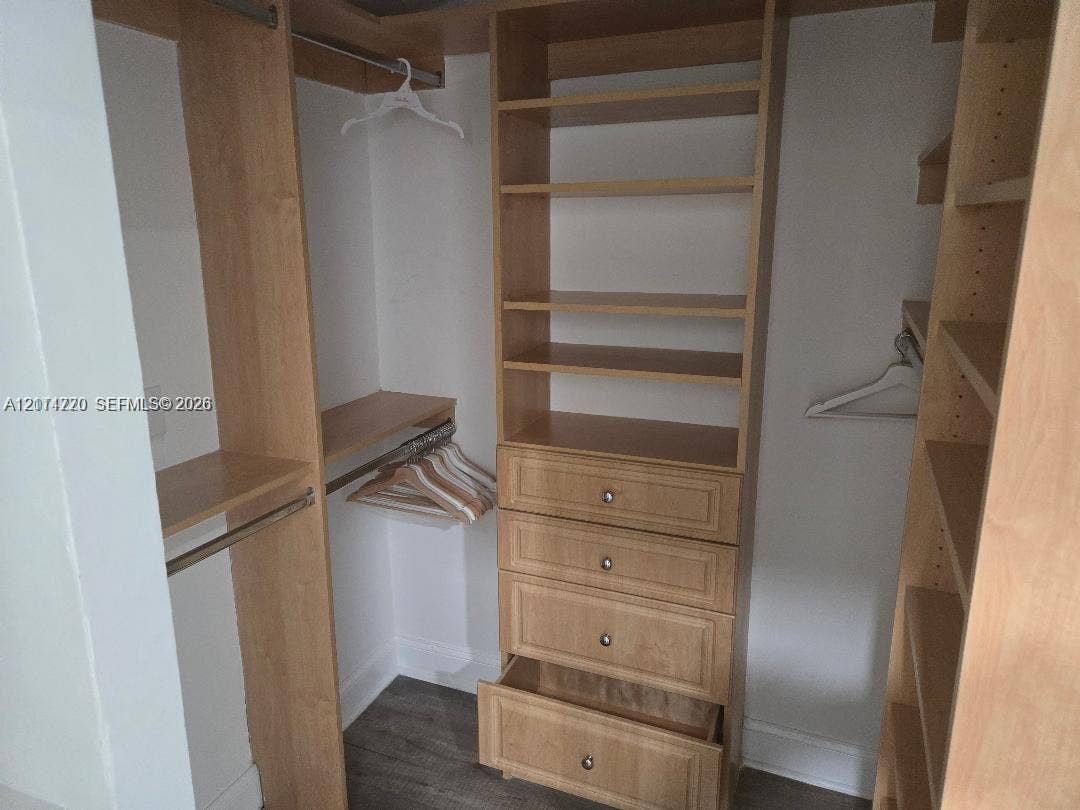 Customized walk-in closet featuring light wood-finish cabinetry, built-in shelving, integrated dresser drawers with metal hardware, and hanging rods