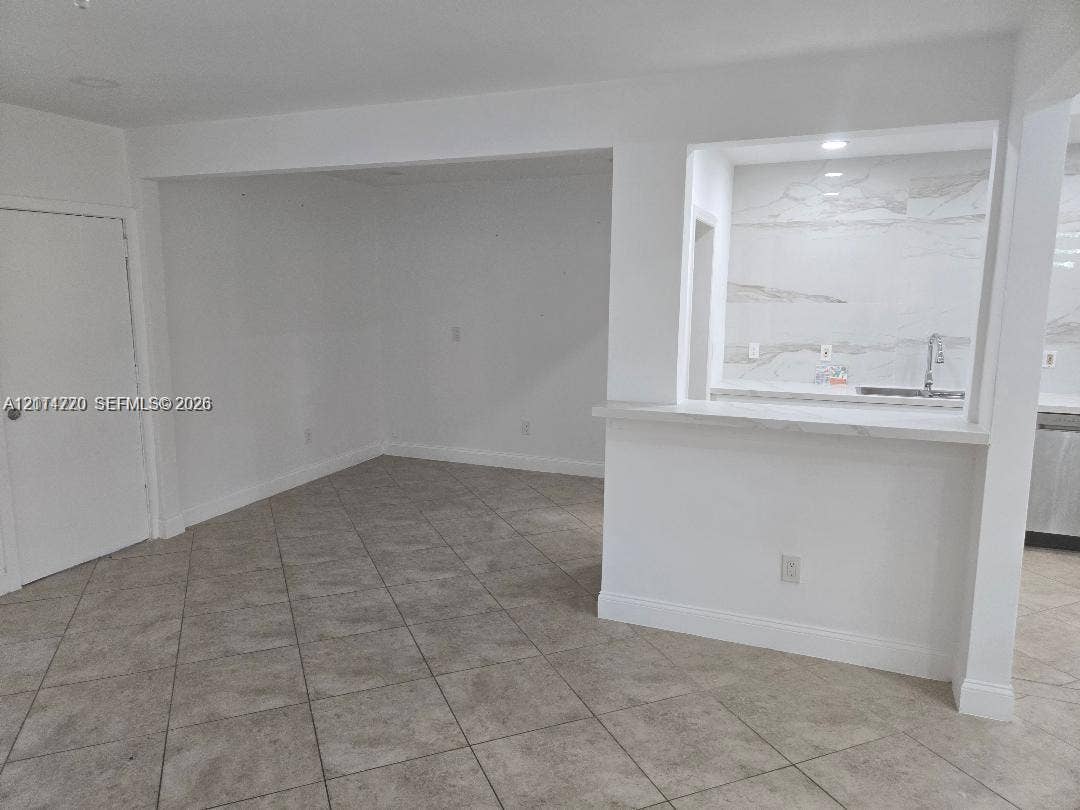 Ceramic tile flooring, pass-through breakfast bar with a stone-finish countertop, and full-height stone-finish backsplash with an undermount sink