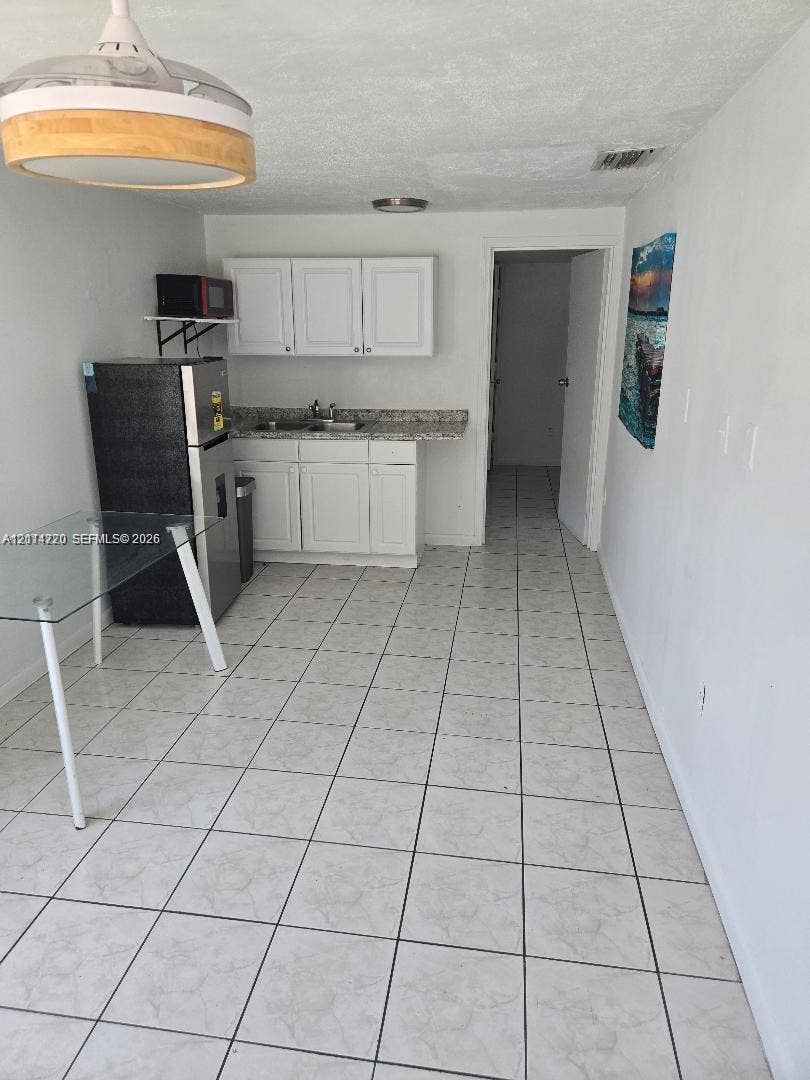 Kitchenette featuring white cabinetry, stone-finish countertops, ceramic tile flooring, and a pendant ceiling light fixture