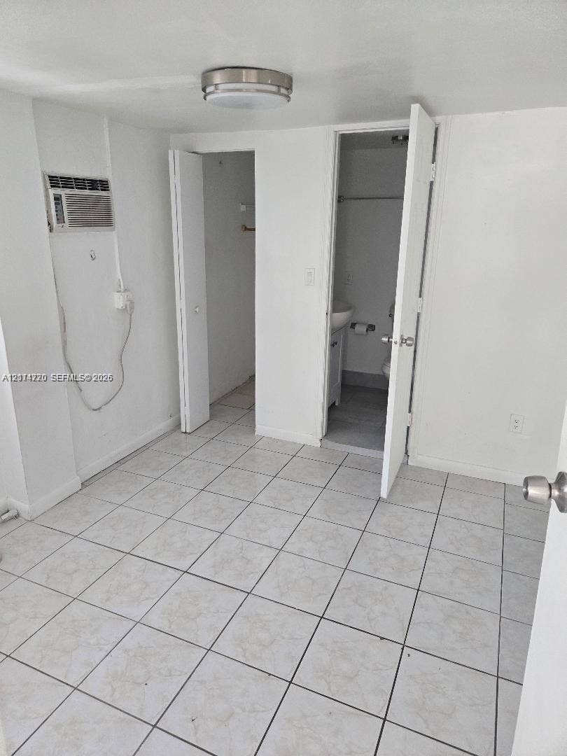 Room featuring neutral tile flooring, a wall-mounted cooling unit, ceiling-mounted lighting, and double-door closet storage