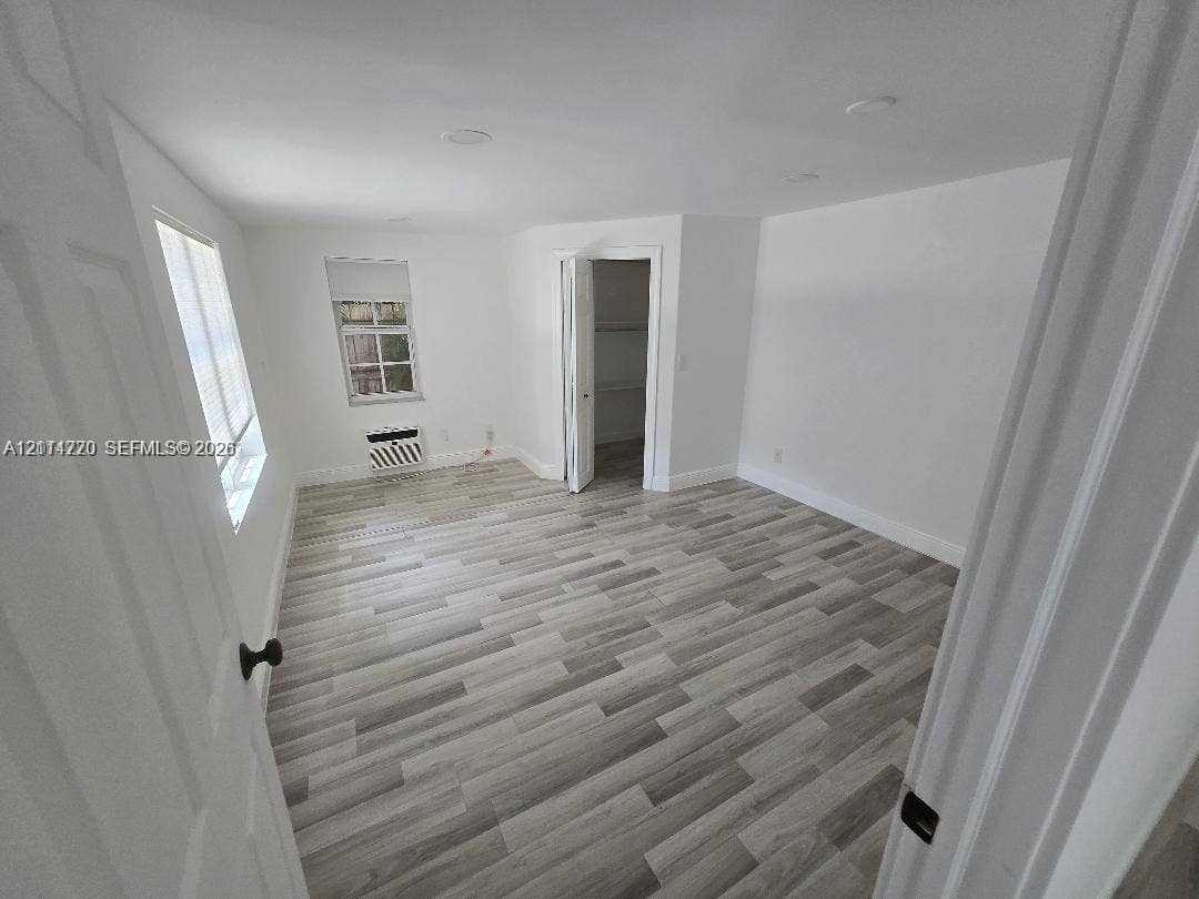 Interior room featuring wood-finish flooring, recessed ceiling lighting, a dedicated closet with built-in shelving, and a wall-mounted air conditioning unit