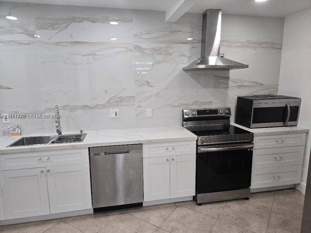 Kitchen featuring white cabinetry, large-format stone-patterned tile backsplash, stainless steel appliances, and solid surface countertops