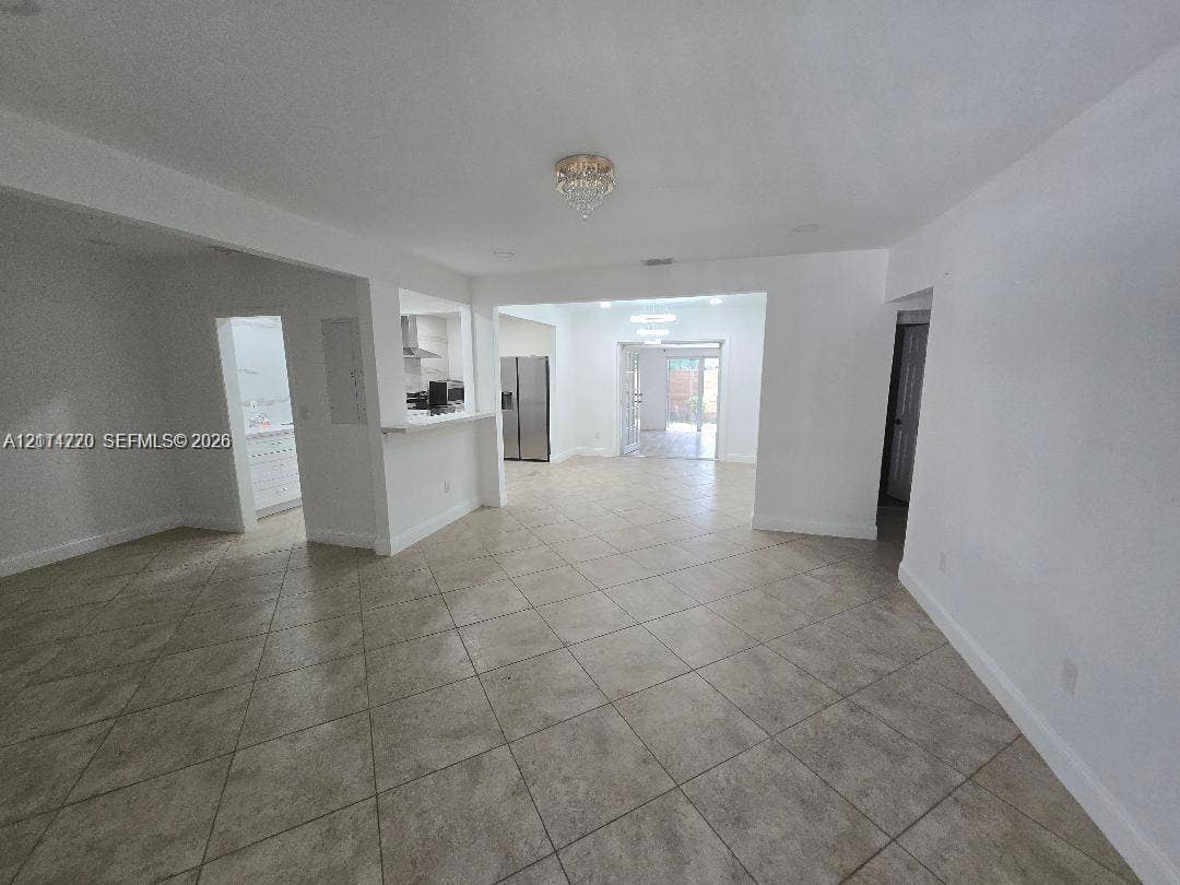 Open-concept interior featuring large-format neutral floor tile, recessed lighting, breakfast bar, and glass-paneled exterior door