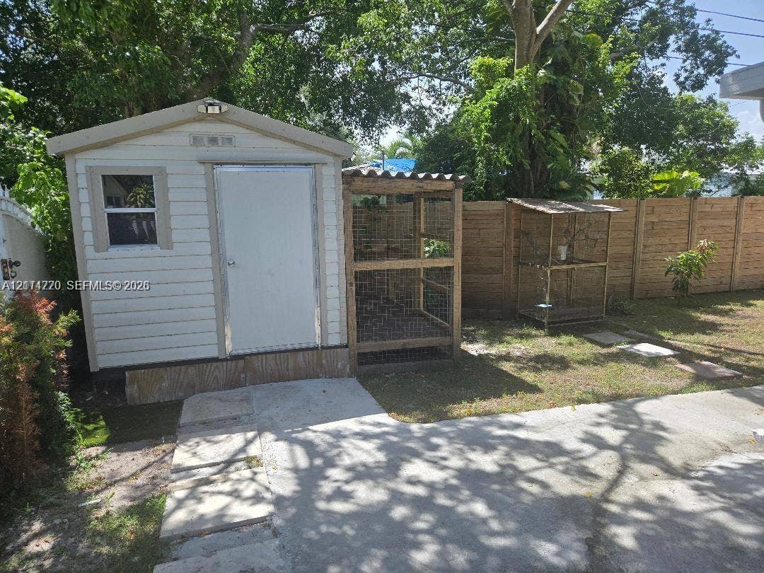 Outdoor storage shed featuring horizontal siding, a single-entry door, and an attached wire-mesh enclosure, set within a fenced perimeter