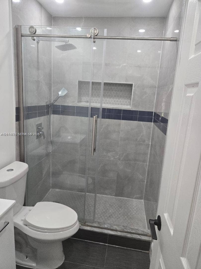 Walk-in shower featuring a sliding glass enclosure, rainfall showerhead, integrated tiled wall niche, and contrasting decorative accent tile