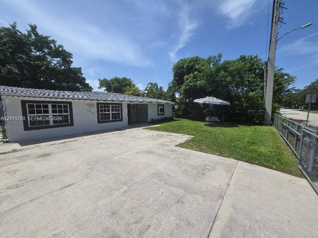 Single-story residence featuring a concrete driveway, grid-pattern windows, a hip roof, and a lawn enclosed by chain-link fencing