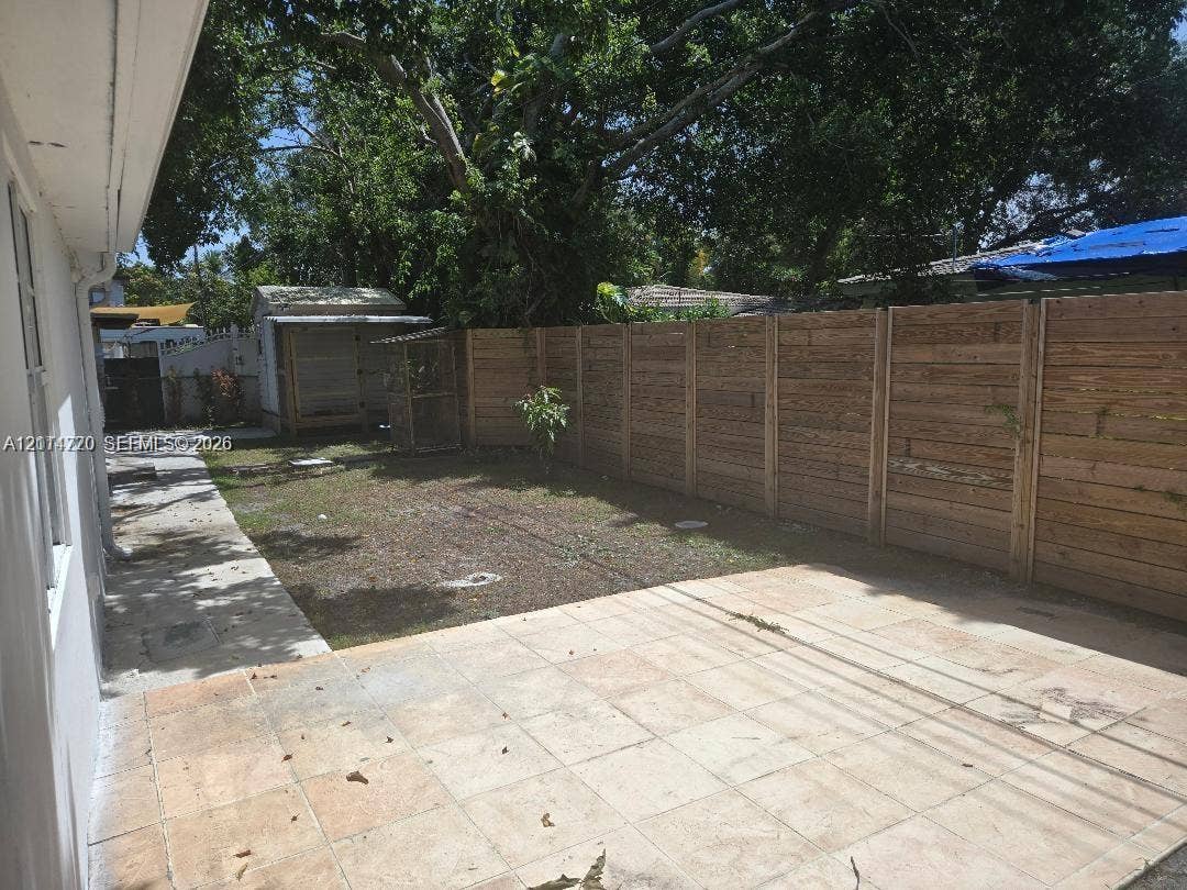 Rear outdoor space featuring a paved tile patio, a horizontal wood-slat privacy fence, and an integrated exterior storage structure