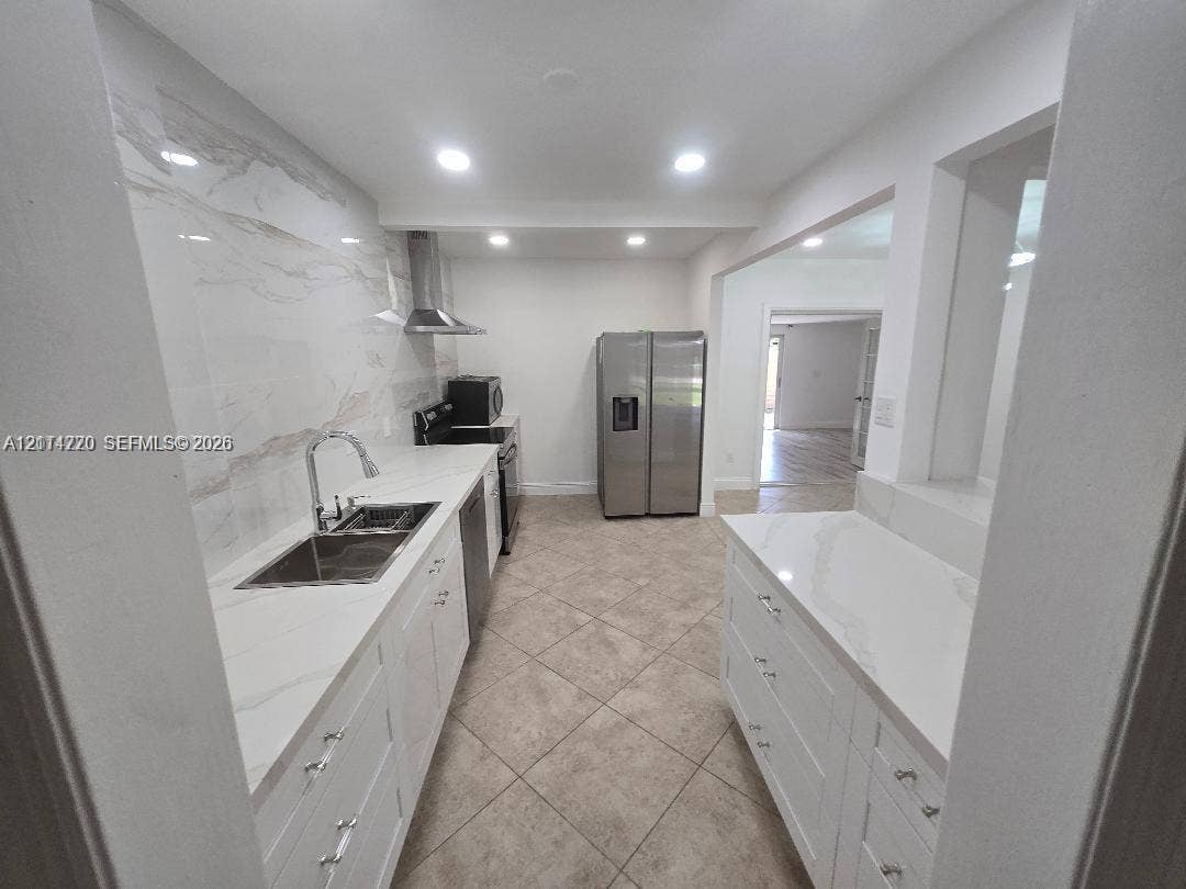 Kitchen featuring white shaker-style cabinetry, quartz countertops, full-height stone-look backsplash, stainless steel appliances, and tile flooring
