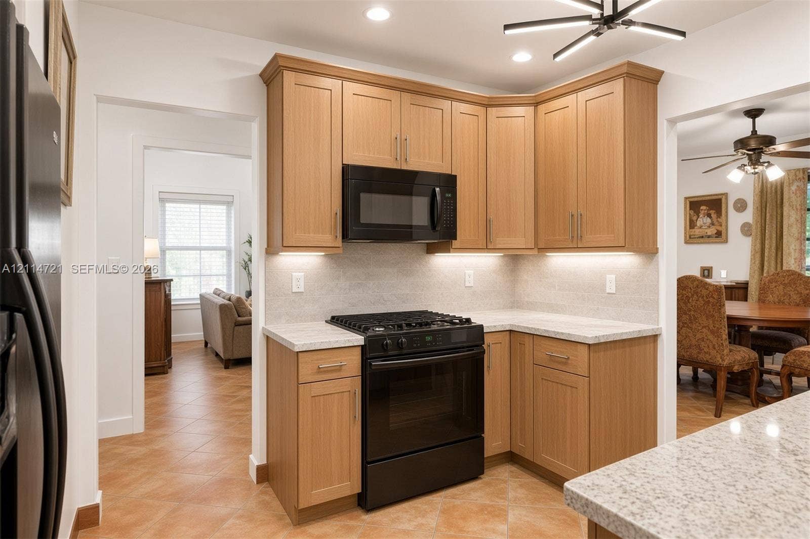 Kitchen featuring light-finish cabinetry, stone-texture countertops, integrated under-cabinet lighting, black gas range with matching microwave, and geometric overhead lighting fixture