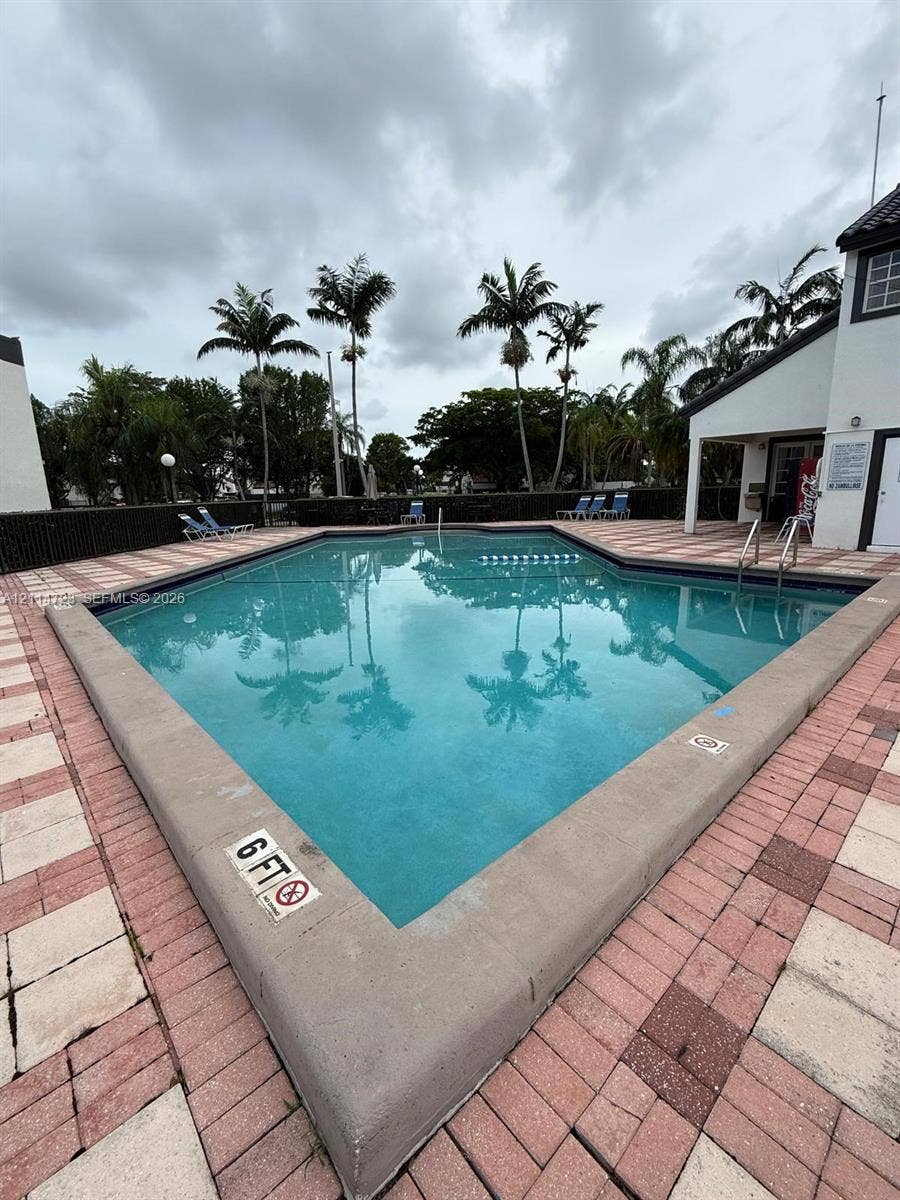 In-ground swimming pool featuring a concrete coping, patterned paver deck, metal ladder, and perimeter landscaping