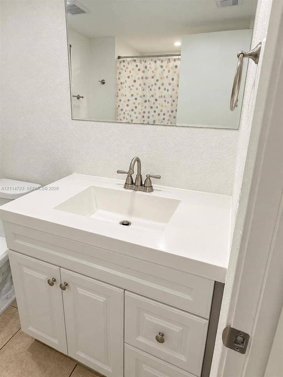 White vanity featuring a solid-surface countertop with an integrated rectangular sink and brushed nickel hardware