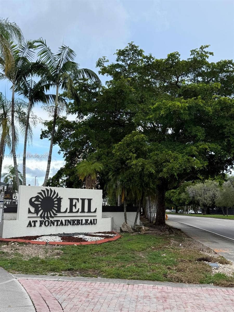 Community monument sign featuring dimensional lettering, decorative landscaping with ground cover, and mature palm and hardwood trees