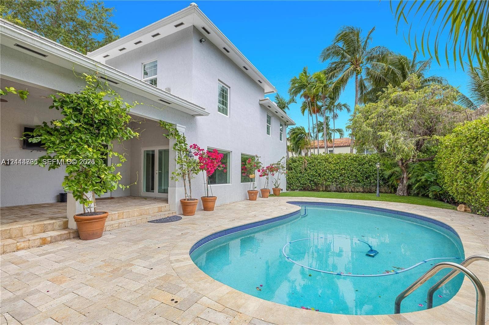 Covered terrace with stone tile flooring, freeform swimming pool, and manicured privacy hedge