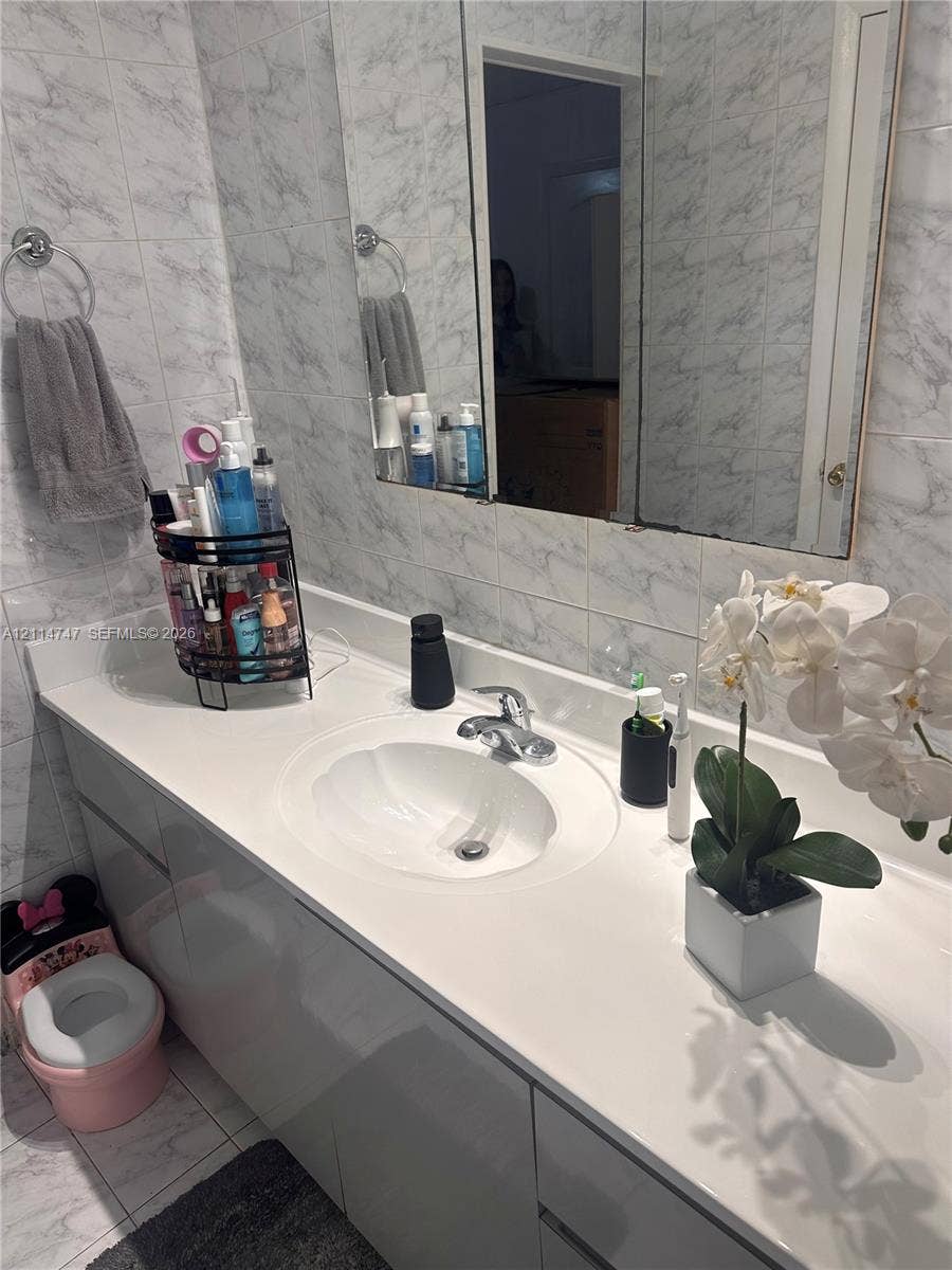 1285 W 26th Place, #202, Hialeah, Hialeah, FL 33010 Bathroom vanity featuring a solid-surface countertop with an integrated oval sink, chrome faucet, mirrored medicine cabinet, and wall-to-wall light-toned tiling