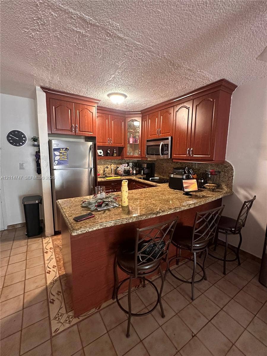 1285 W 26th Place, #202, Hialeah, Hialeah, FL 33010 Kitchen featuring raised-panel wood cabinetry, natural stone countertops, integrated breakfast bar, and stainless steel built-in microwave
