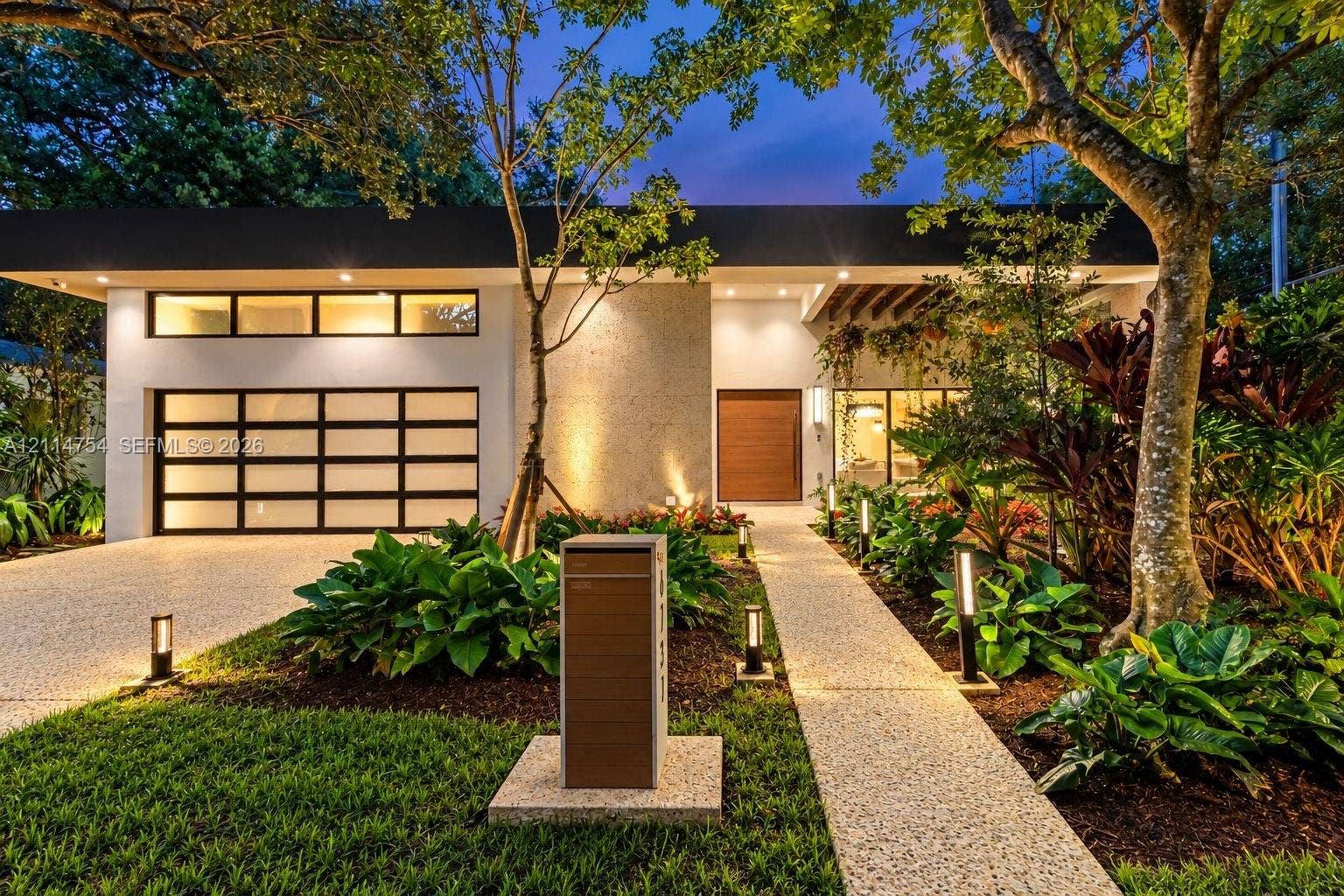 6731 SW 64th Avenue, South Miami, FL 33143 Modern single-story exterior featuring a smooth stucco facade, sectional frosted glass garage door, textured stone accent wall, wood-finish entry door, and exposed timber ceiling beams